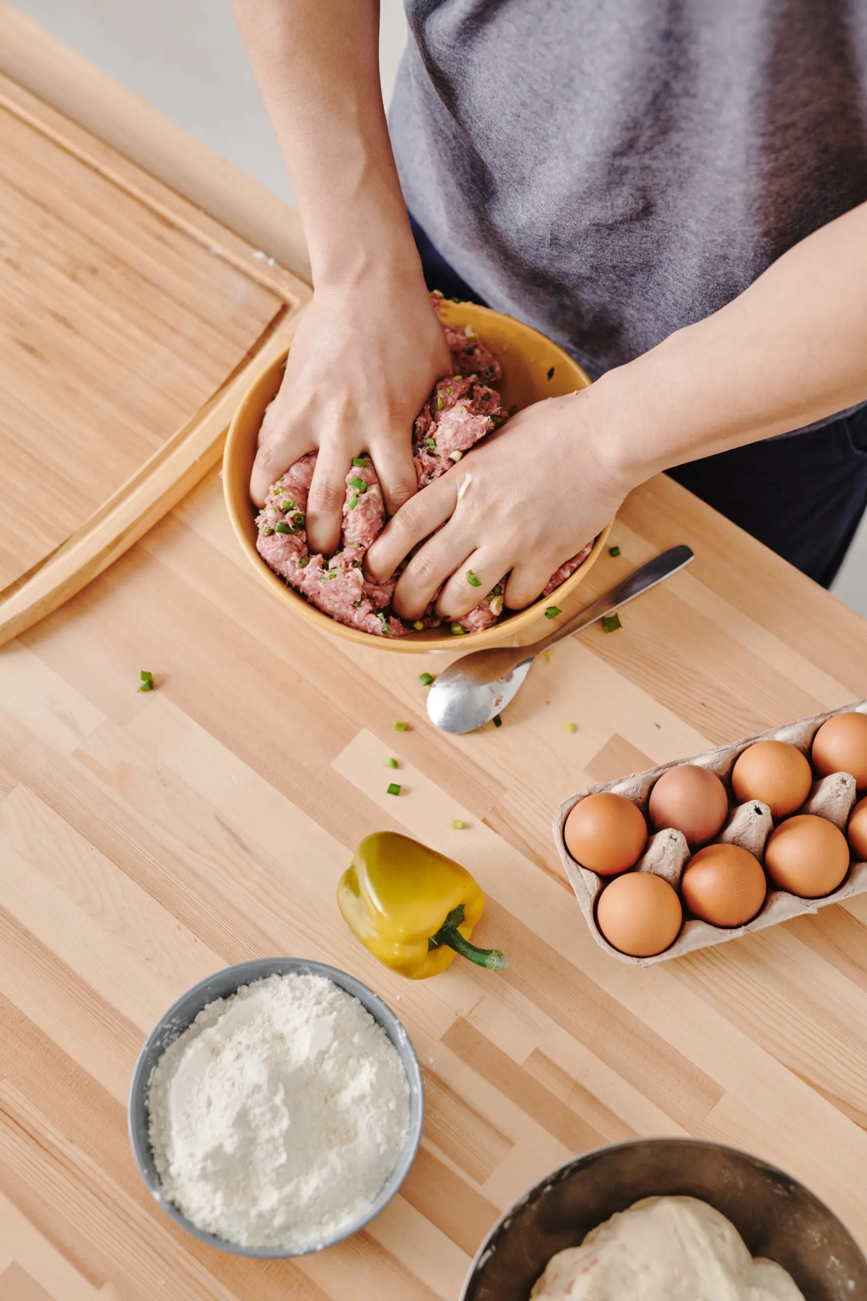 Vitamin B12: Wichtige Informationen und Tipps für Sie 1 Person knetet Hackfleisch mit frischen Zutaten in einer Küche, umgeben von Eiern, Mehl und Paprika – Lebensmittel reich an Folsäure (Vitamin B9).