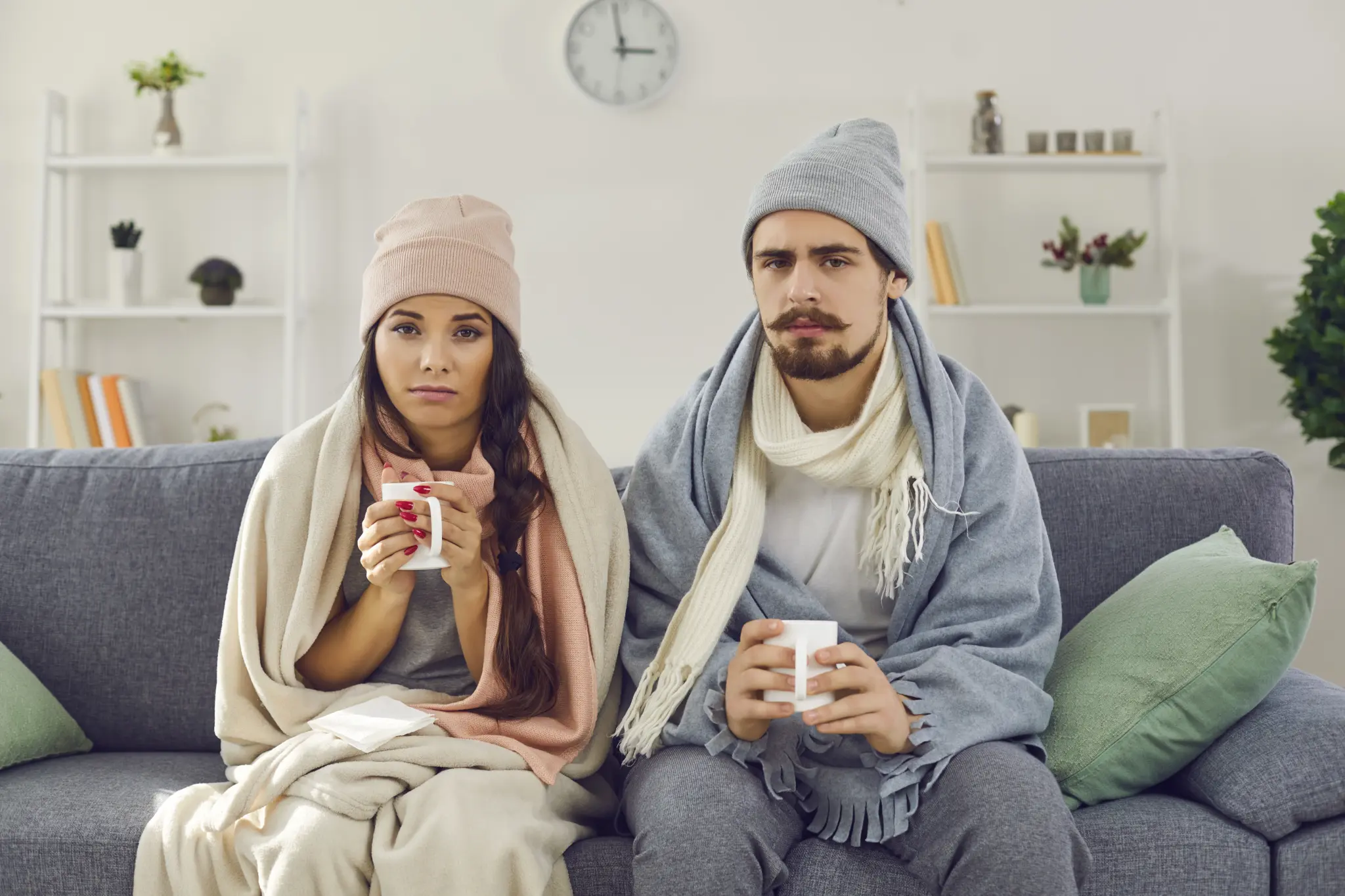 Grippeimpfung: 7 Überraschende Nebenwirkungen 2024 23 Zwei erkältete Personen in Decken gehüllt, trinken Tee auf einem Sofa – Immunsystem stärken bei Hausarztpraxis München am Romanplatz, Grippe, Grippe Impfung, Influenza Impfung