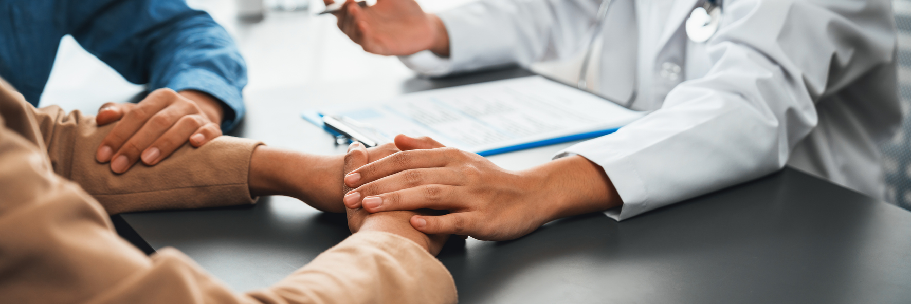 Arzt legt beruhigend die Hand auf die Hand eines Patienten – vertrauensvolle Allgemeinmedizin in München