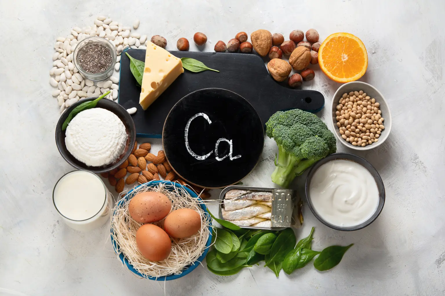 Calcium und Vitamin im Körper für starke Knochen & Muskeln! 50 Verschiedene calciumreiche Lebensmittel wie Käse, Brokkoli, Mandeln, Eier, Joghurt, Spinat, weiße Bohnen, Chiasamen, Orangen und Sardinen auf einem Tisch arrangiert, Calcium, Calcium Mangel Symptome, Calcium Mangel